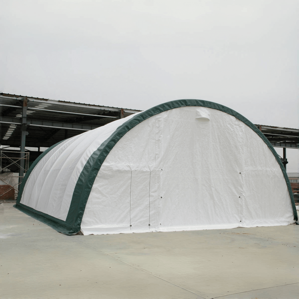 White and green arched storage shelter with single truss design on concrete surface
