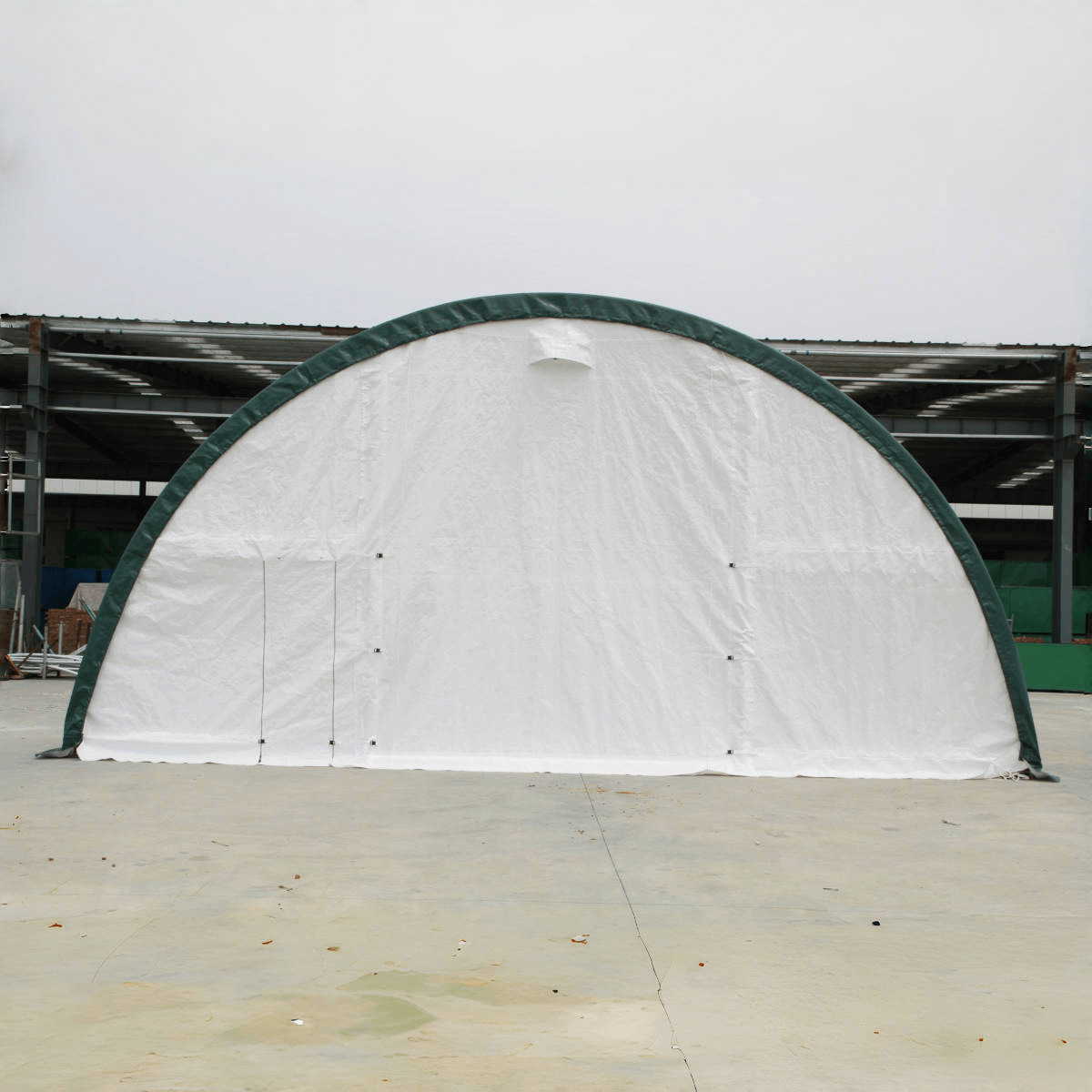 White fabric dome-shaped storage shelter with green metal arch frame on concrete surface